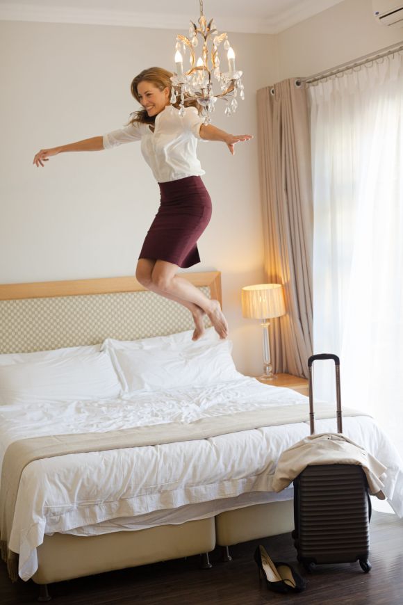 Donna d'affari che salta sul letto in una stanza d'albergo